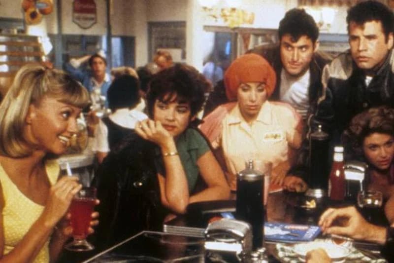 The cast of Grease sitting around malt shop table